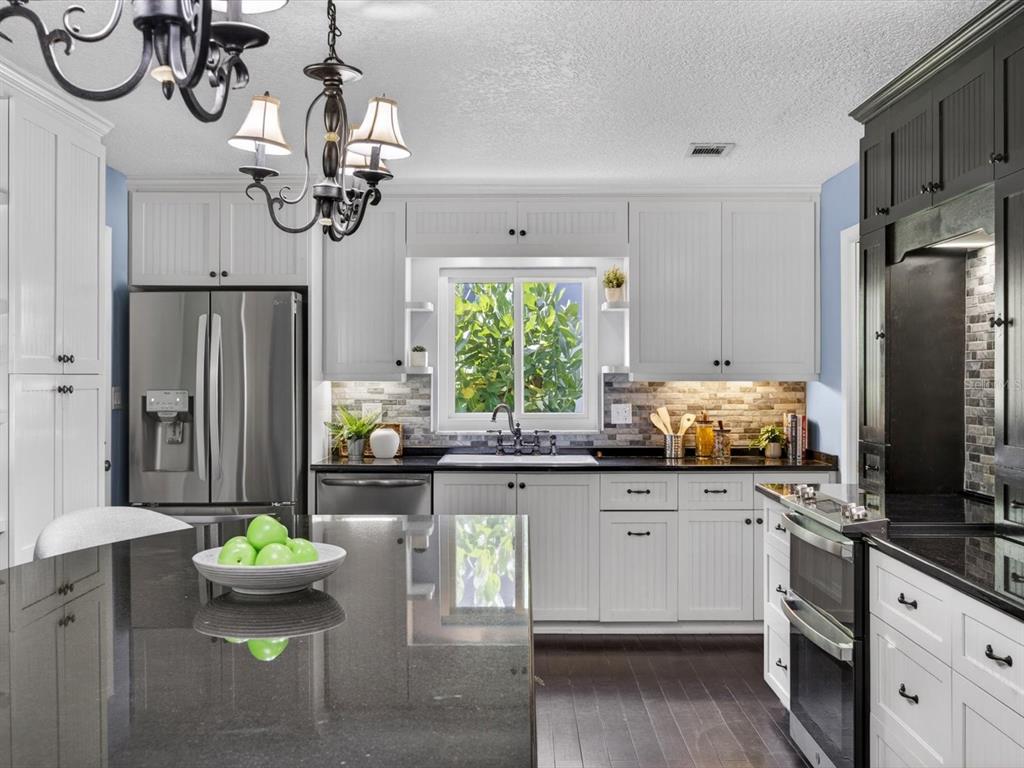 A kitchen features white cabinets, black countertops, a kitchen island, and a stainless steel refrigerator — 333 CORNWALL ROAD, WINTER PARK, FL
