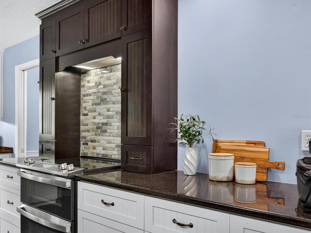 A kitchen features dark brown upper cabinets, white lower cabinets, and a stone tile backsplash — 333 CORNWALL ROAD, WINTER PARK, FL
