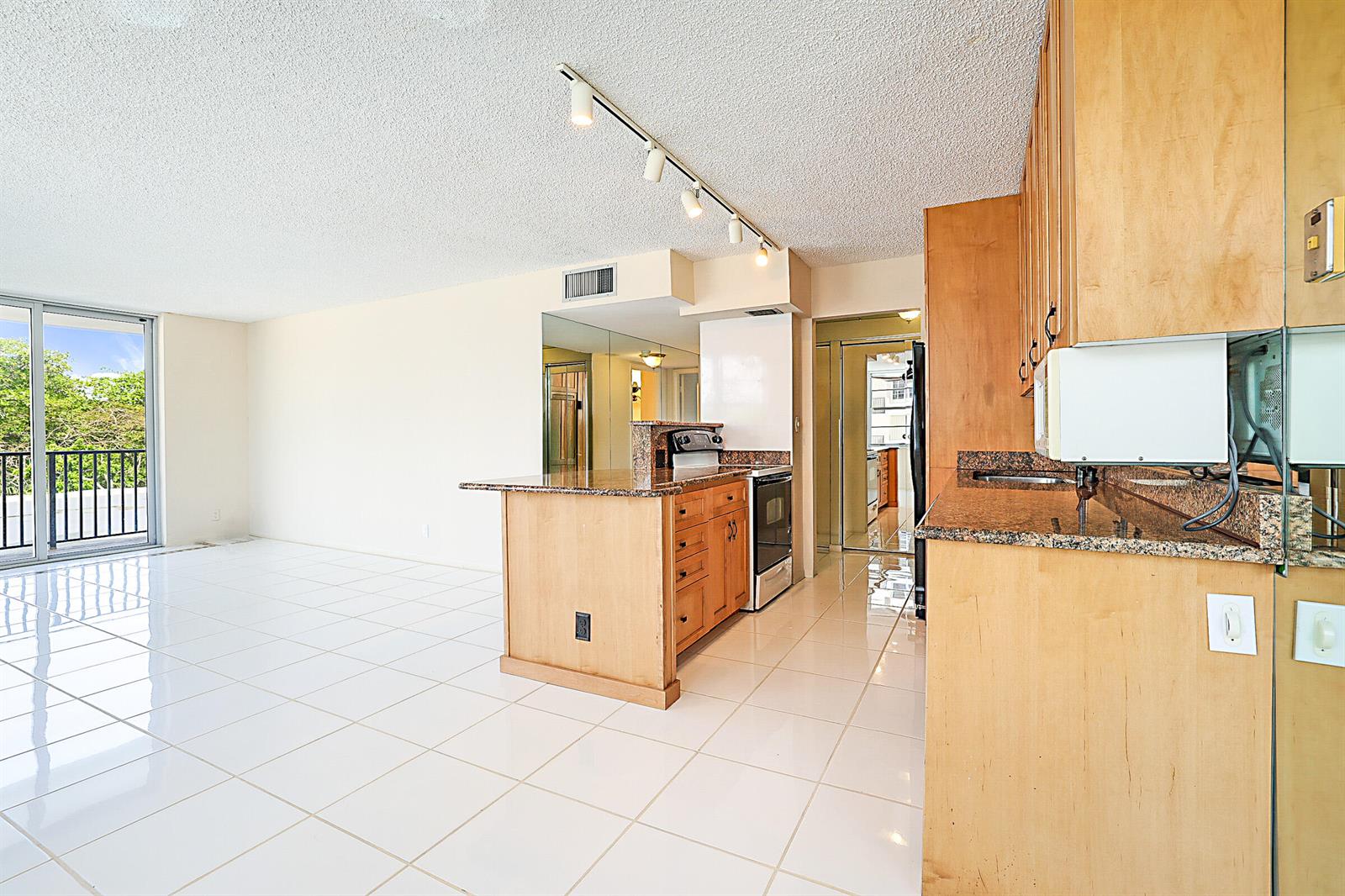 A kitchen with light wood cabinets and granite countertops opens to a bright living area — 2121 N Ocean Boulevard # 302e, Boca Raton FL 33431, BOCA RATON, FL