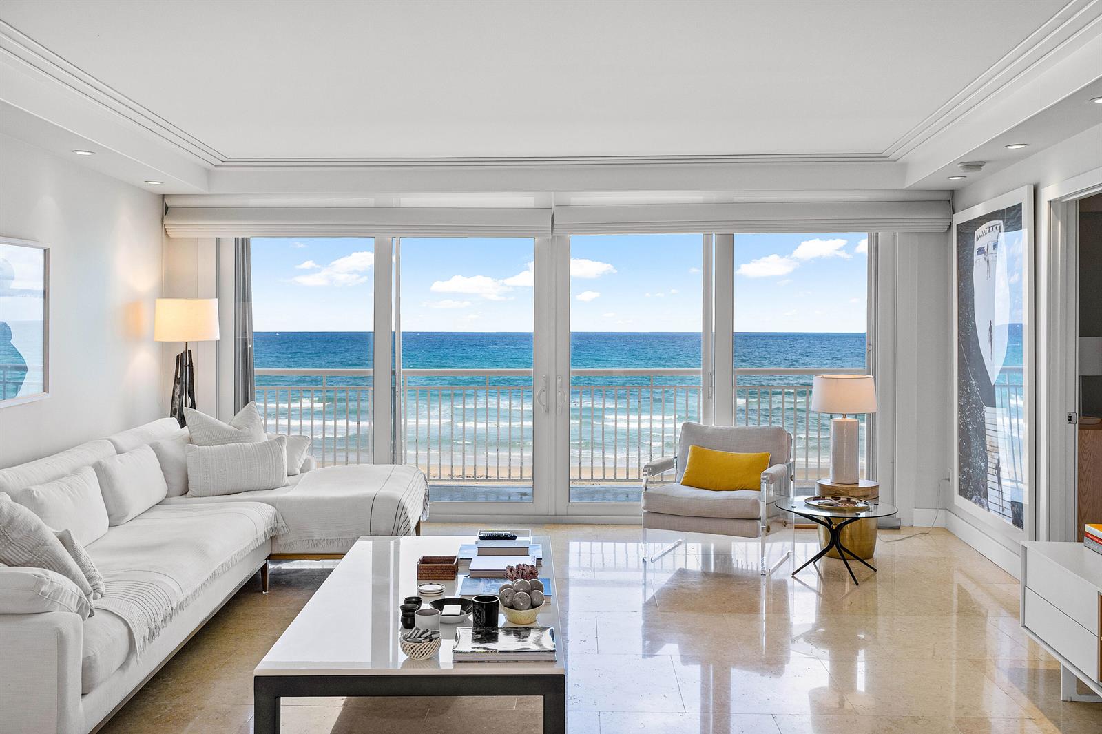 A bright living room features white furniture, a glass coffee table, and floor-to-ceiling ocean views — 2780 S Ocean Boulevard # 401, Palm Beach FL 33480, PALM BEACH, FL