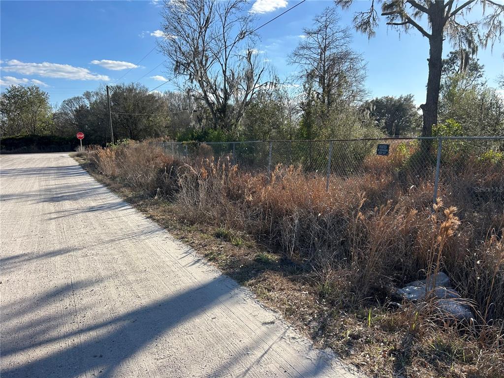 A dirt road runs alongside a chain-link fence bordering a vacant, overgrown lot — 6000 US HIGHWAY 98 W, FROSTPROOF, FL