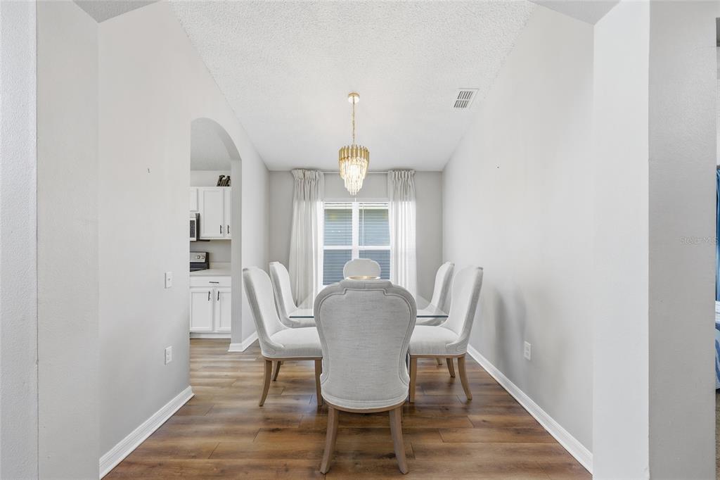 A dining room features light gray walls, wood-look flooring, a glass table, and a chandelier — 440 LANGHAM DRIVE, DAVENPORT, FL