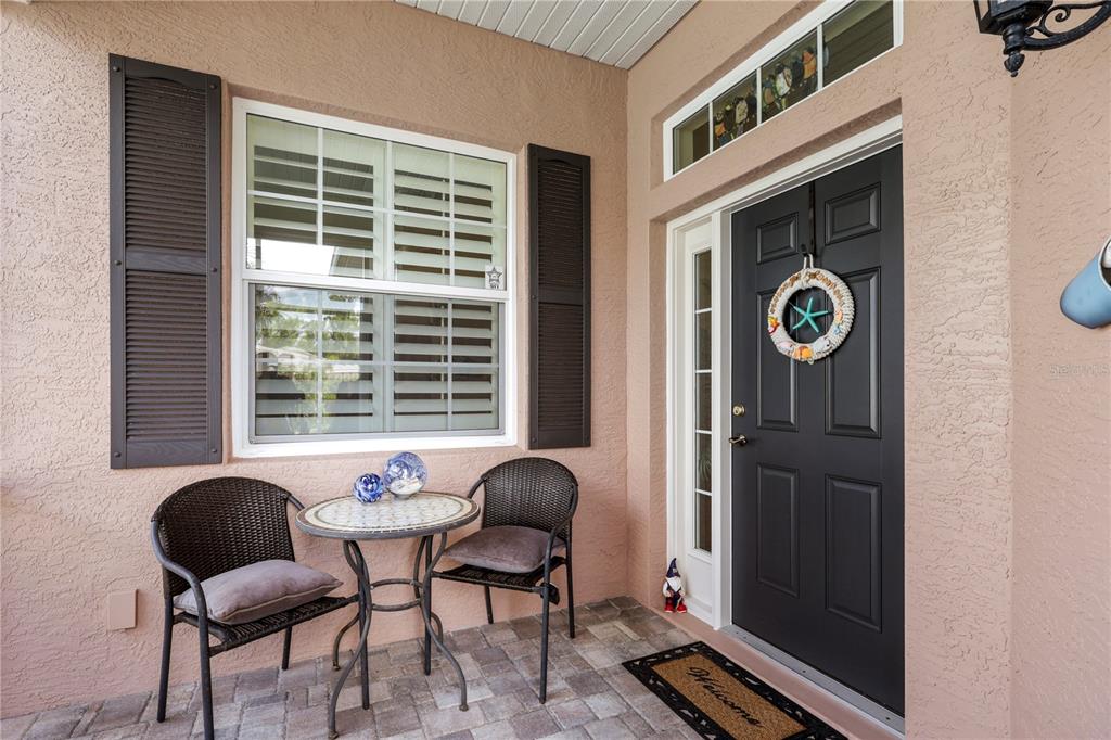 A front porch features a dark door with a wreath, two wicker chairs, and a table — 1848 LANCASHIRE DRIVE UNIT 1848, VENICE, FL