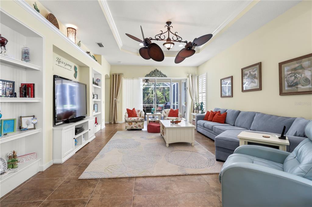 A living room features a sectional sofa, a television, built-in shelving, and a ceiling fan — 1848 LANCASHIRE DRIVE UNIT 1848, VENICE, FL