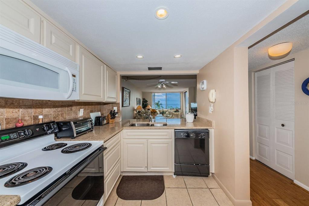 A kitchen with white cabinets, a black dishwasher, and a view into the living area — 6218 PALMA DEL MAR BOULEVARD S UNIT 401, ST PETERSBURG, FL