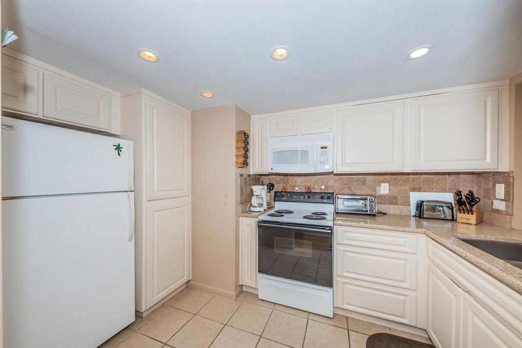 A kitchen with white cabinets, a white refrigerator, a white stove, and tan tile flooring — 6218 PALMA DEL MAR BOULEVARD S UNIT 401, ST PETERSBURG, FL