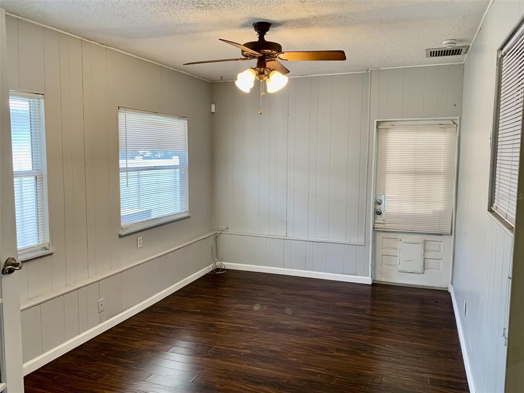 An empty room with gray paneled walls, dark wood flooring, a ceiling fan, and windows — 5050 29TH AVENUE N, ST PETERSBURG, FL