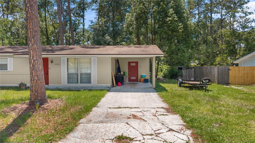 A single-story house with a beige exterior, a red front door, and a concrete carport — 5030 NW 28TH TERRACE, GAINESVILLE, FL