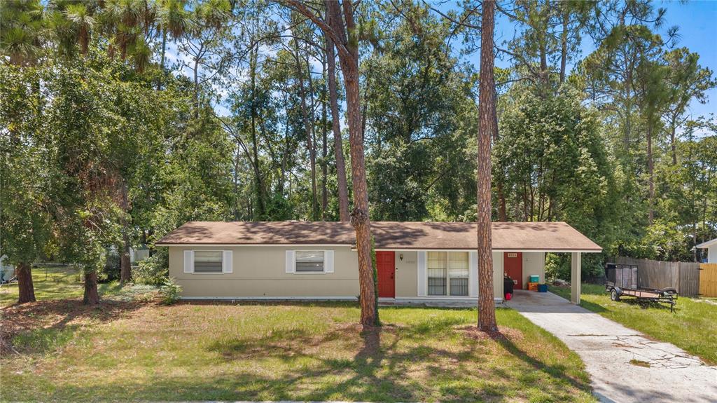 A single-story house with a beige exterior, a red front door, and an attached carport — 5030 NW 28TH TERRACE, GAINESVILLE, FL