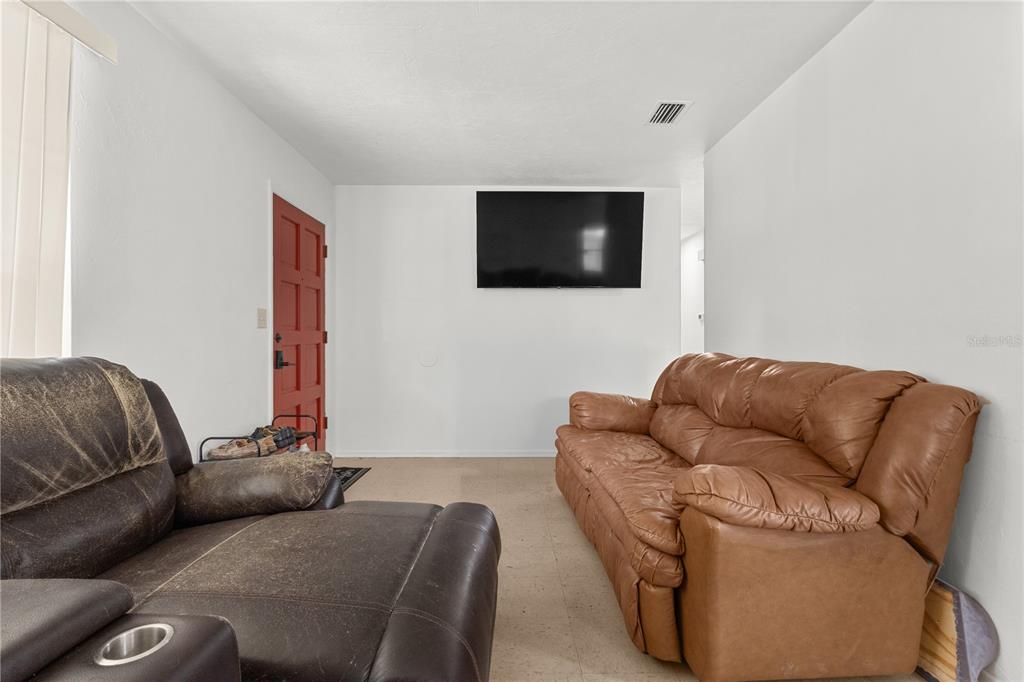 A living room features a brown leather sofa, a recliner, and a wall-mounted television — 5030 NW 28TH TERRACE, GAINESVILLE, FL