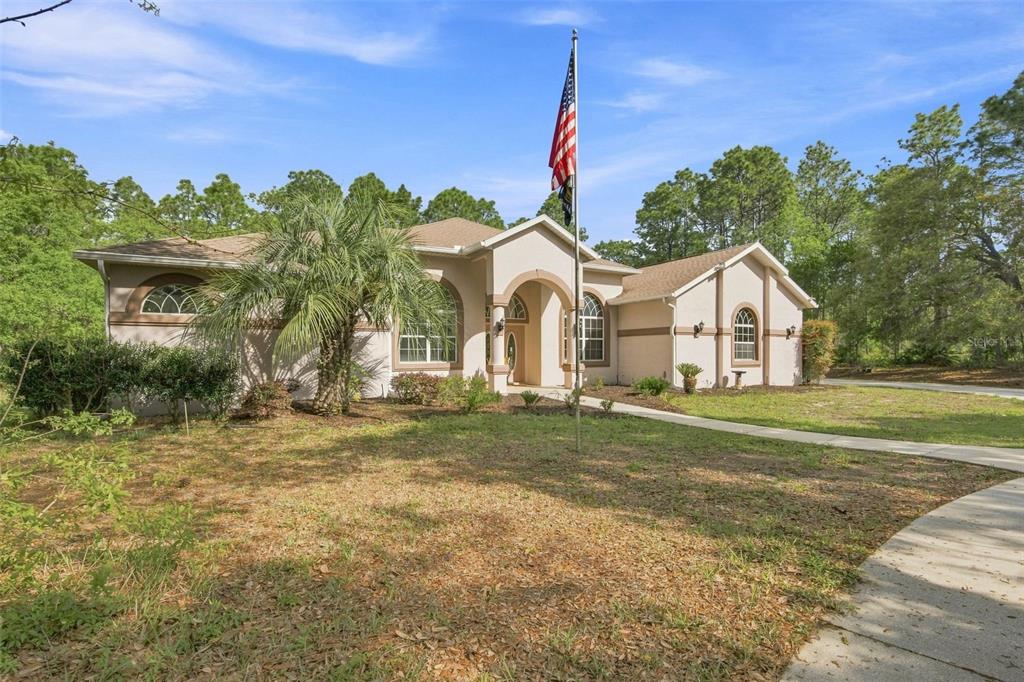 A single-story beige house with a palm tree and an American flag in the front yard — 3210 N RENO WAY, BEVERLY HILLS, FL