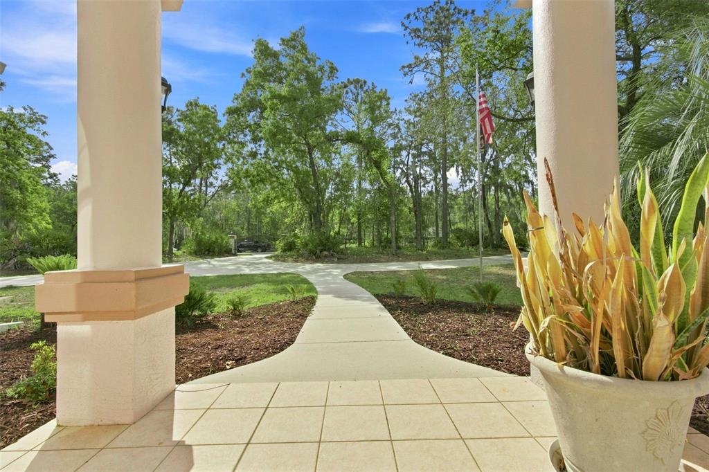 A view from a tiled porch looking out toward a driveway, trees, and a flagpole — 3210 N RENO WAY, BEVERLY HILLS, FL