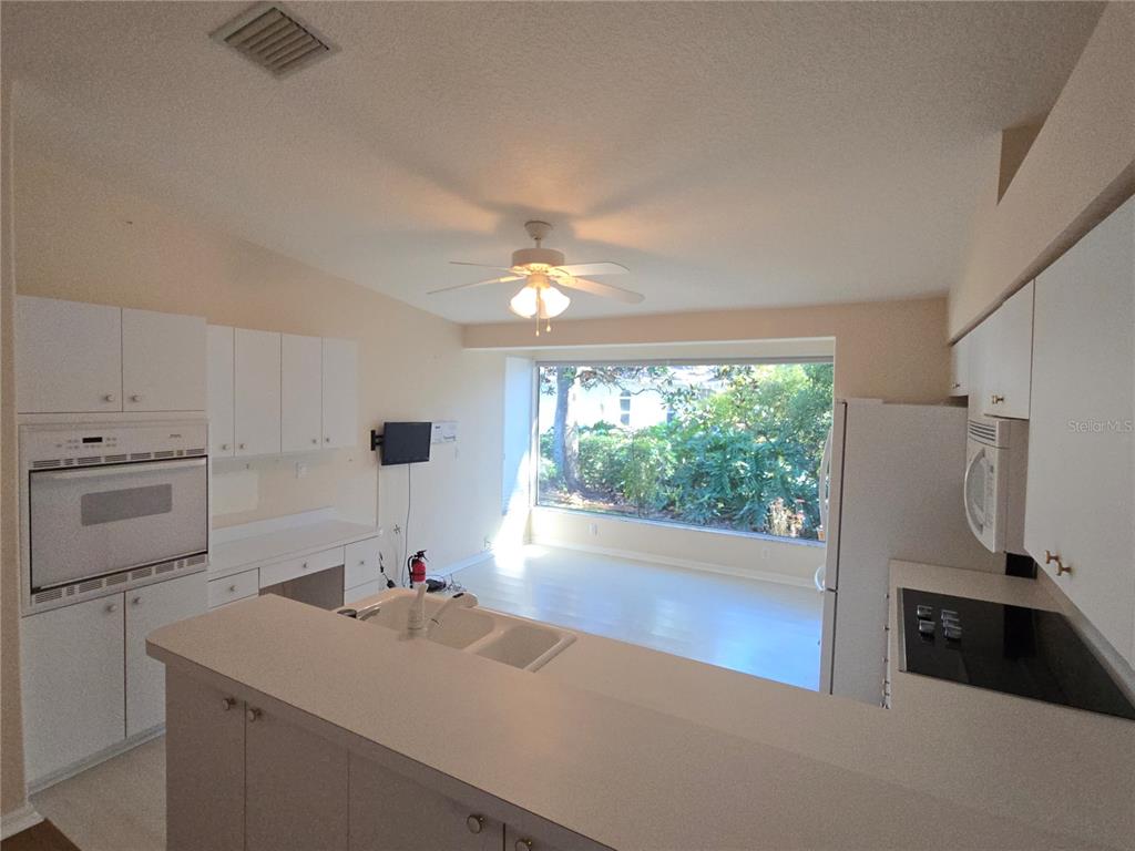 A kitchen with white cabinets and appliances overlooks a bright living area with large windows — 11519 HOLLY ANN DRIVE, NEW PORT RICHEY, FL