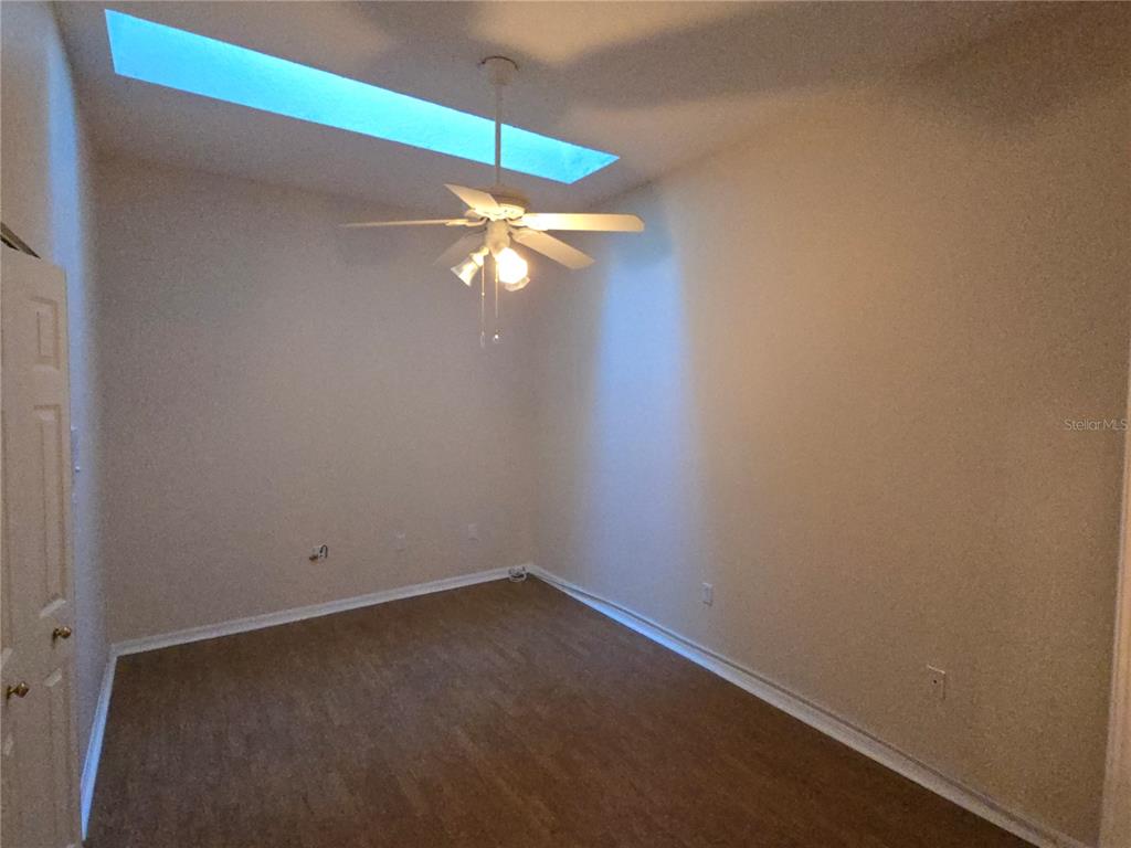 An empty room features a ceiling fan, a skylight, and wood-look flooring — 11519 HOLLY ANN DRIVE, NEW PORT RICHEY, FL