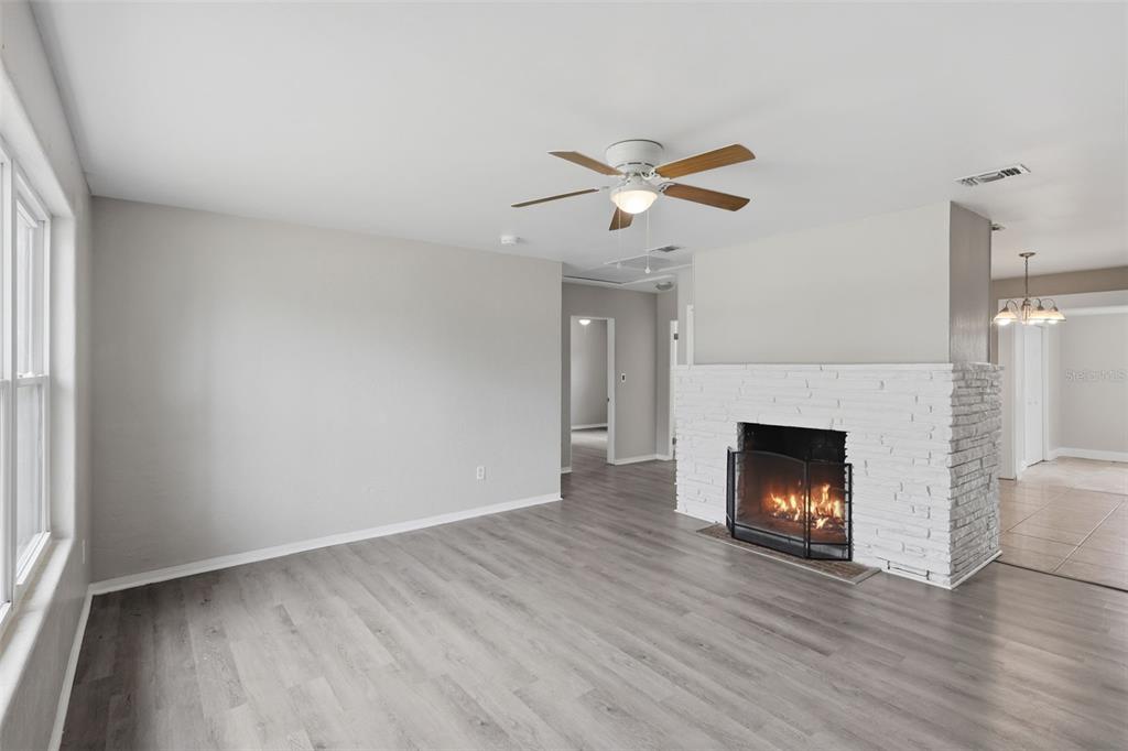 A living room features gray wood-look flooring, a white brick fireplace, and a ceiling fan — 748 COLFAX DRIVE, DAYTONA BEACH, FL