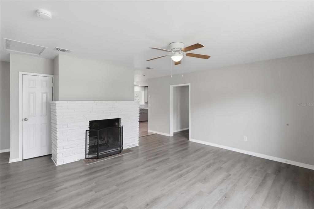 A living room features gray wood-look flooring, a white brick fireplace, and a ceiling fan — 748 COLFAX DRIVE, DAYTONA BEACH, FL