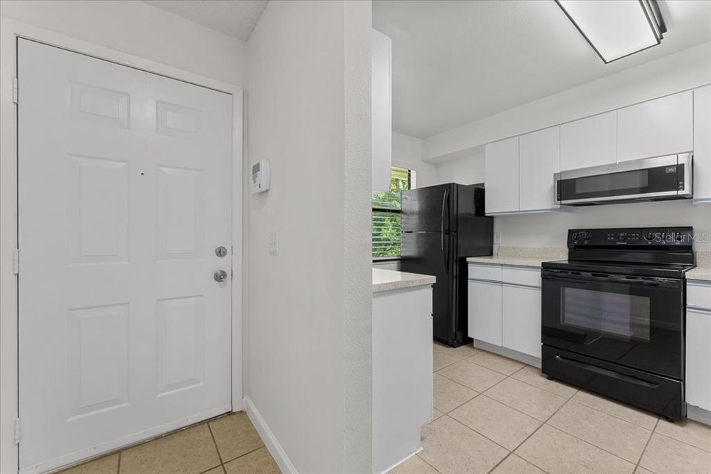 A kitchen with white cabinets, black appliances, and tile flooring next to an entryway door — 3001 58TH AVENUE S UNIT 1106, ST PETERSBURG, FL