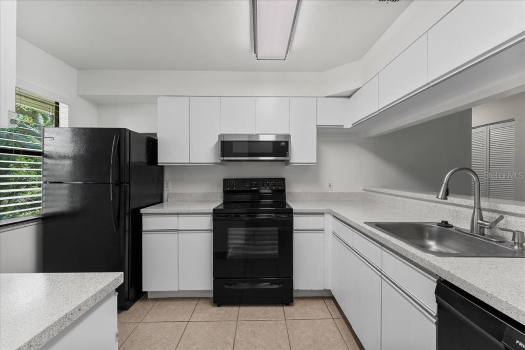 A kitchen features white cabinets, black appliances, light countertops, and tile flooring — 3001 58TH AVENUE S UNIT 1106, ST PETERSBURG, FL