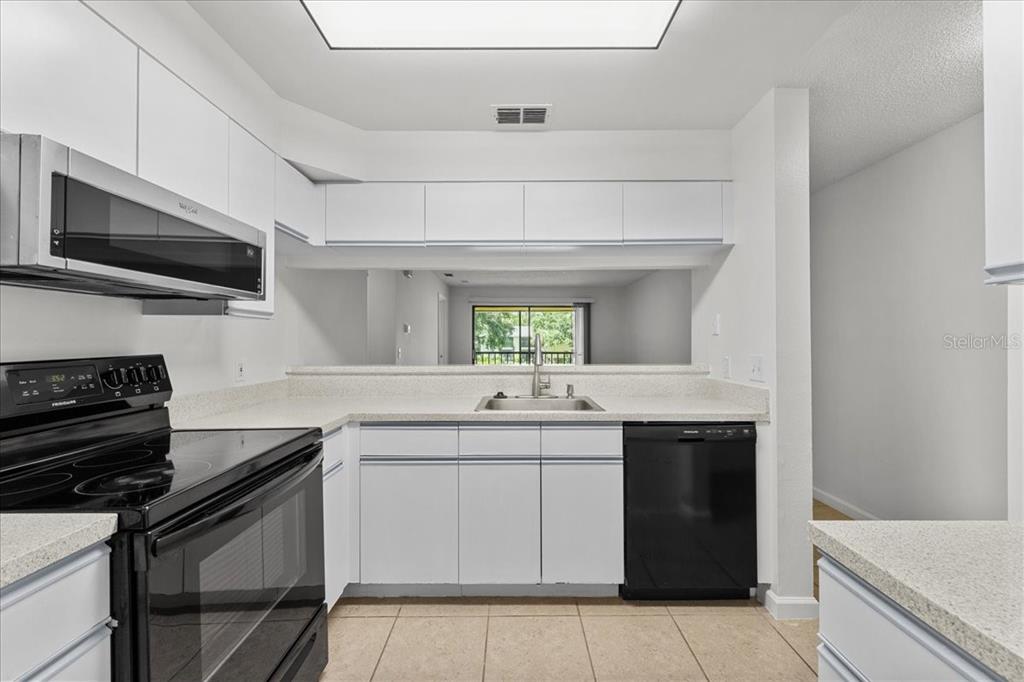 A kitchen features white cabinets, black appliances, a pass-through window, and light-colored tile flooring — 3001 58TH AVENUE S UNIT 1106, ST PETERSBURG, FL