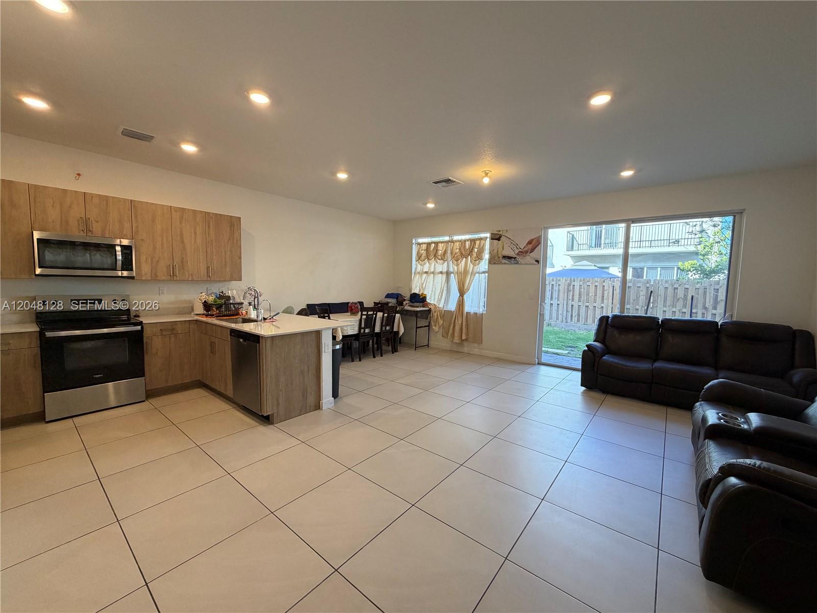 An open-concept kitchen and living area features light tile flooring and a sliding glass door — 159 NE 13th Ter, Homestead FL 33033, HOMESTEAD, FL