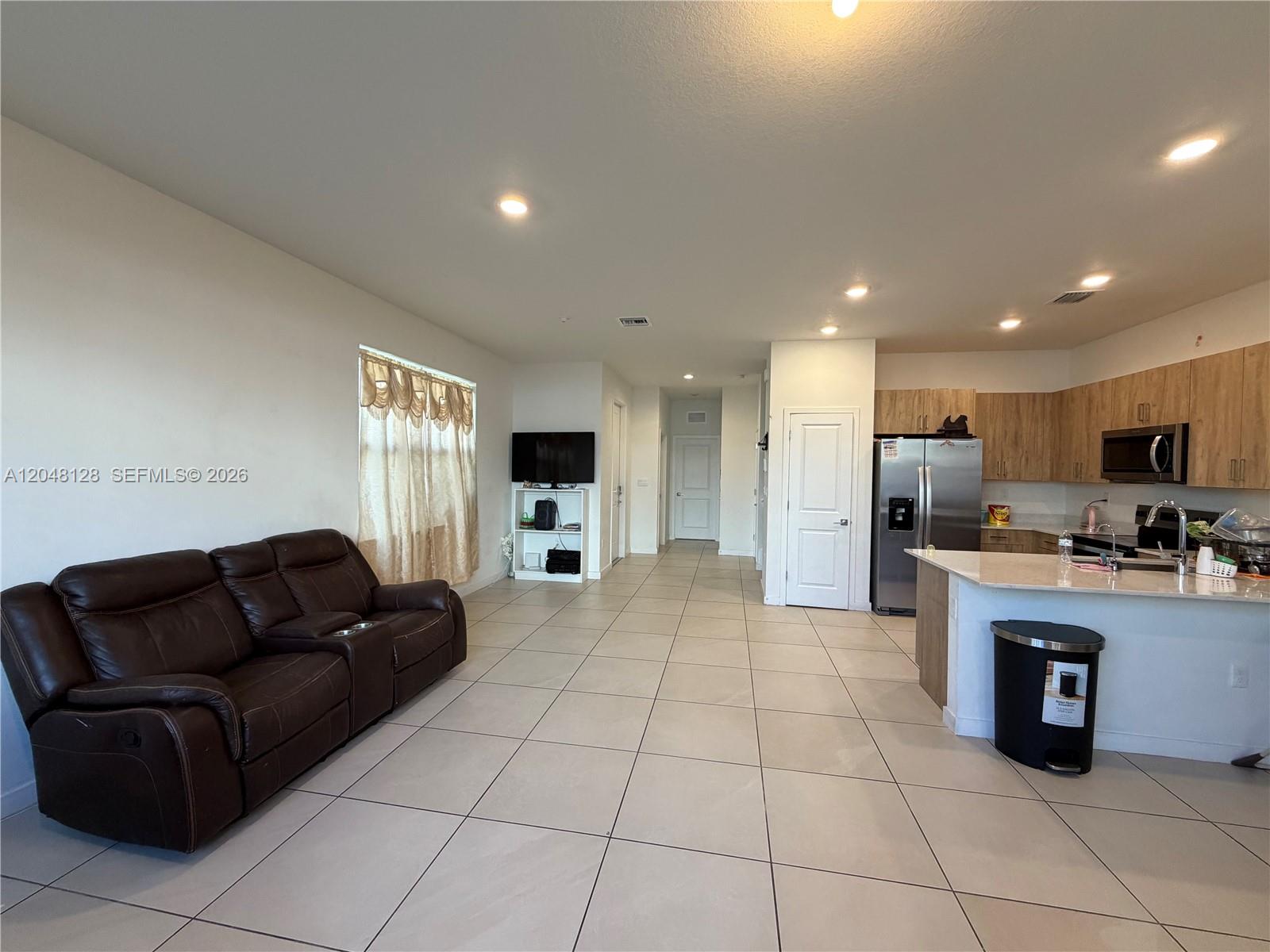 An open-concept living room and kitchen featuring tile flooring and light wood cabinetry — 159 NE 13th Ter, Homestead FL 33033, HOMESTEAD, FL