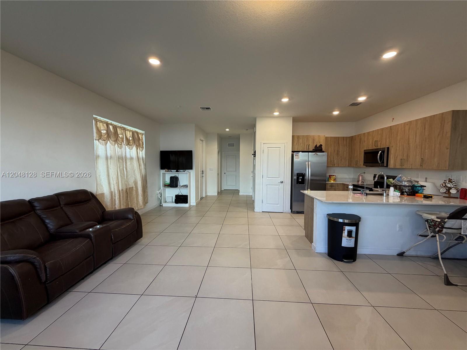 An open-concept living room and kitchen feature light tile flooring and wood-toned cabinetry — 159 NE 13th Ter, Homestead FL 33033, HOMESTEAD, FL