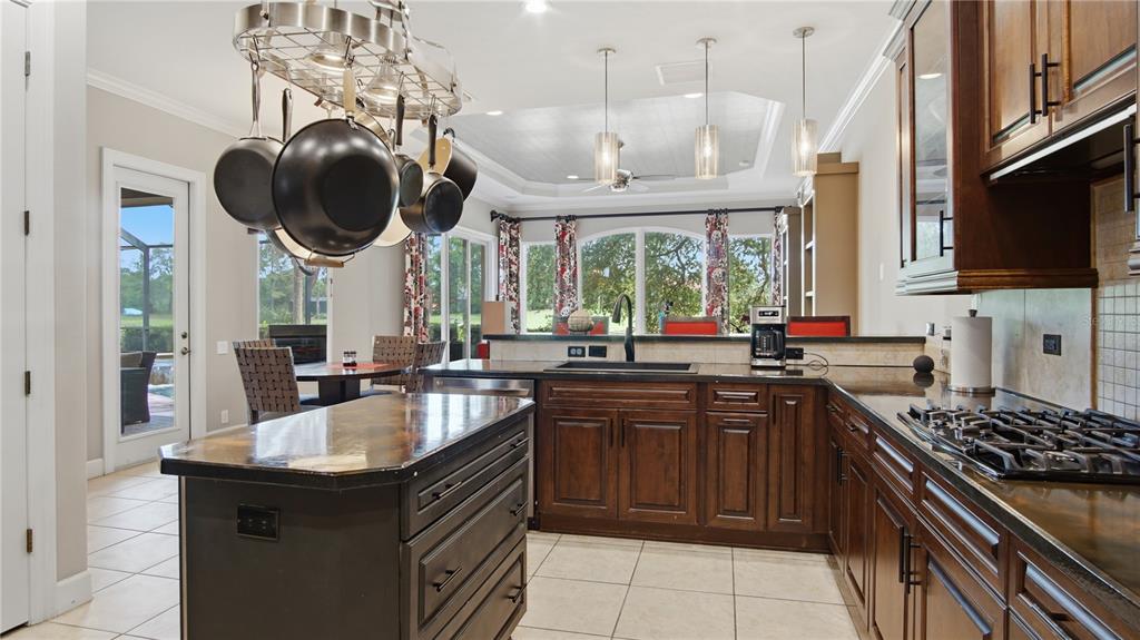 A kitchen features dark wood cabinets, a central island, a hanging pot rack, and tile floors — 6609 SW 179TH AVENUE ROAD, DUNNELLON, FL