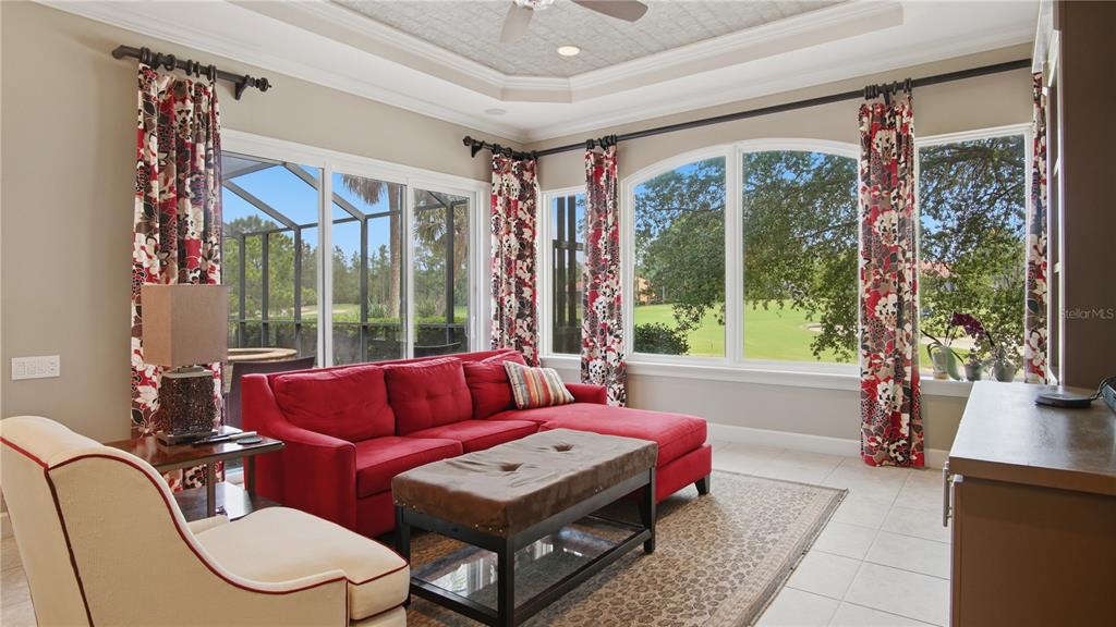 A living room with a red sectional sofa, patterned curtains, and views of a golf course — 6609 SW 179TH AVENUE ROAD, DUNNELLON, FL