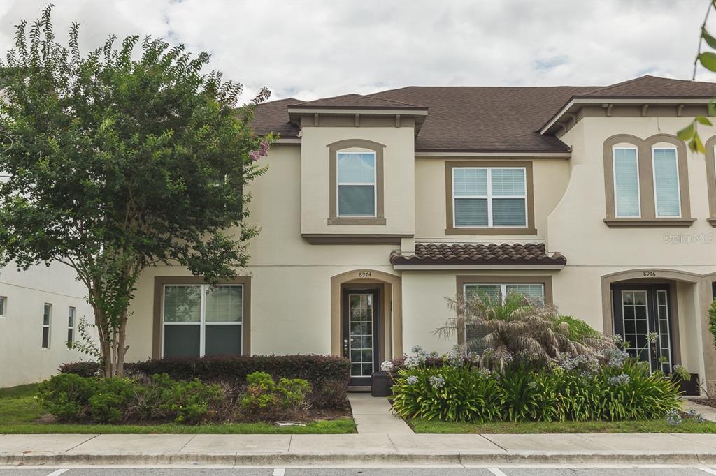 A two-story townhouse exterior with beige stucco walls, brown trim, and a small front garden — 8974 AMELIA DOWNS TRAIL, KISSIMMEE, FL