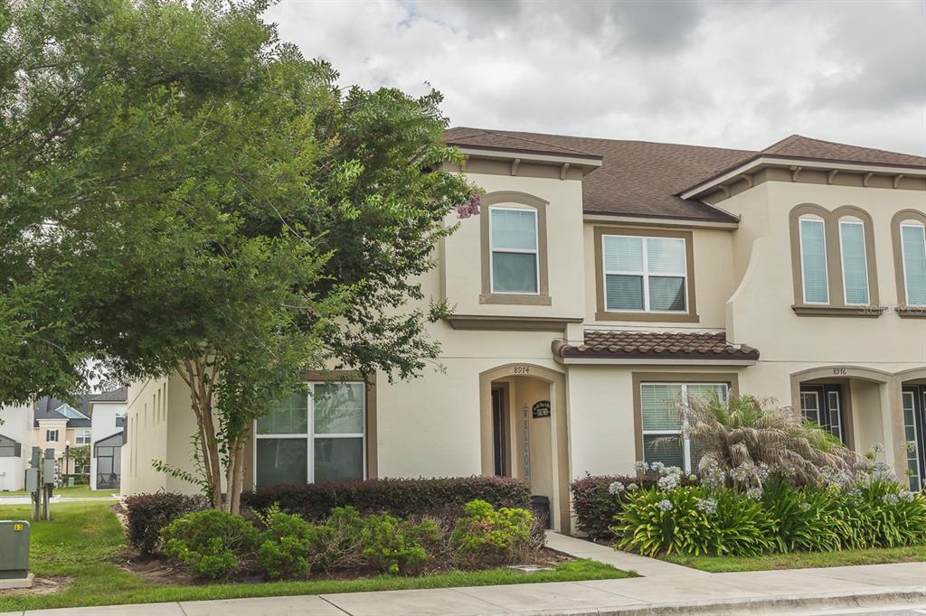 A two-story townhouse with beige stucco siding, a brown shingled roof, and landscaped front yard — 8974 AMELIA DOWNS TRAIL, KISSIMMEE, FL