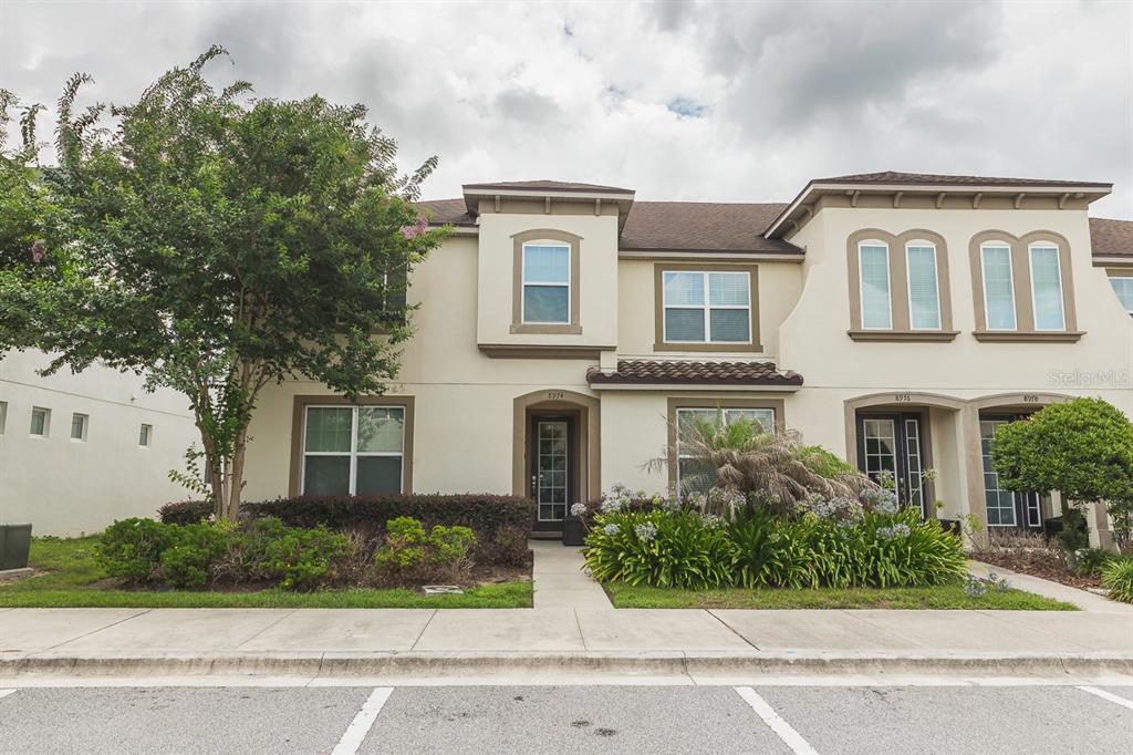 A two-story townhouse exterior with beige stucco walls, a brown shingled roof, and landscaping — 8974 AMELIA DOWNS TRAIL, KISSIMMEE, FL