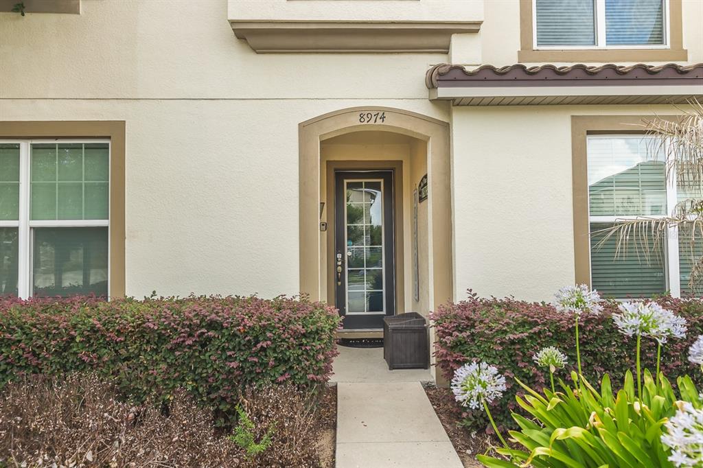 The exterior of a beige two-story home features a front door and landscaped bushes — 8974 AMELIA DOWNS TRAIL, KISSIMMEE, FL