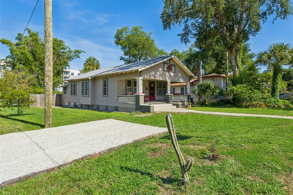 A tan bungalow with a front porch and a gravel driveway sits on a grassy lot — 6002 N SUWANEE AVENUE, TAMPA, FL