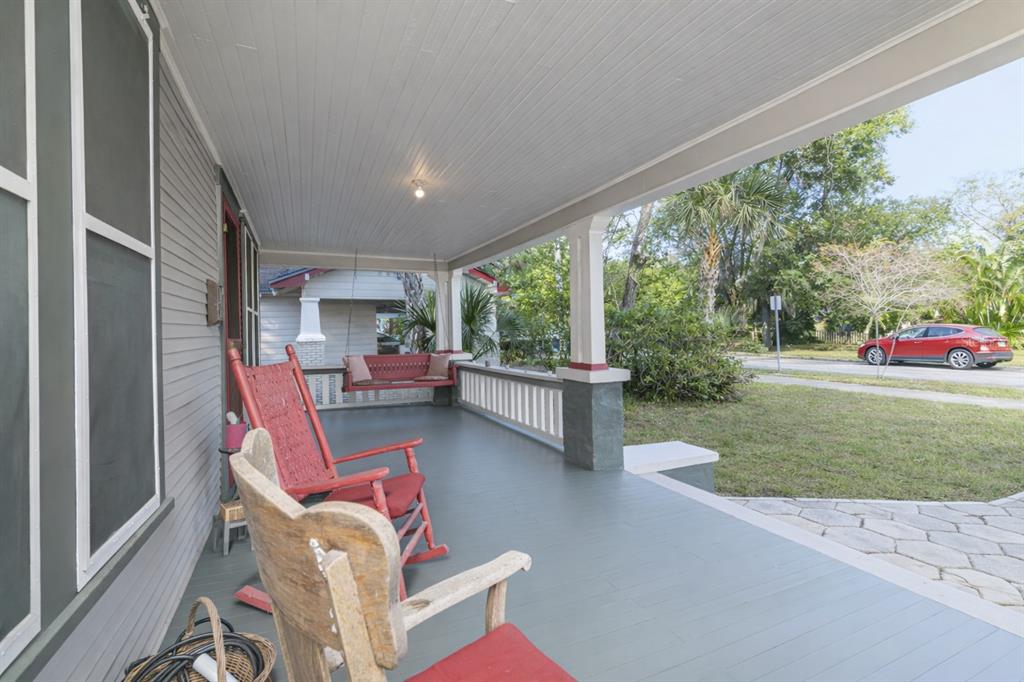 A covered front porch with gray wooden flooring, rocking chairs, and a hanging porch swing — 6002 N SUWANEE AVENUE, TAMPA, FL