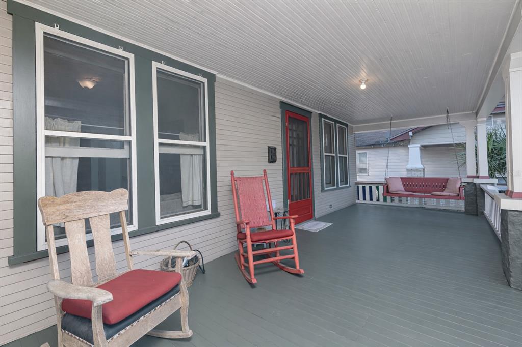 A covered front porch features a wooden rocking chair, a red rocking chair, and a swing — 6002 N SUWANEE AVENUE, TAMPA, FL