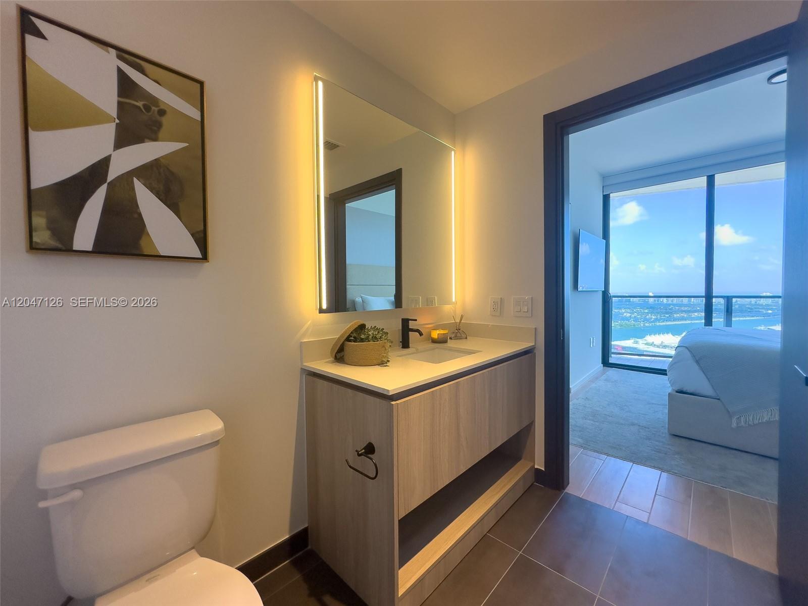 A modern bathroom features a floating wood vanity, illuminated mirror, and a view into a bedroom — 398 NE 5th St # 4210, Miami FL 33132, MIAMI, FL