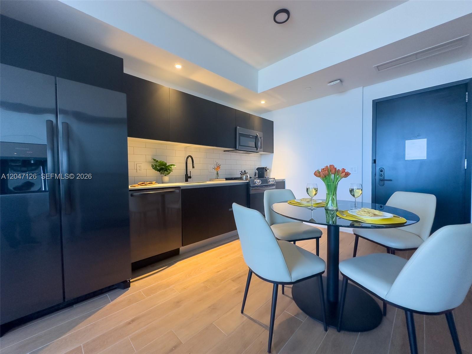 A modern kitchen features dark cabinetry, stainless steel appliances, and a glass-topped dining table — 398 NE 5th St # 4210, Miami FL 33132, MIAMI, FL