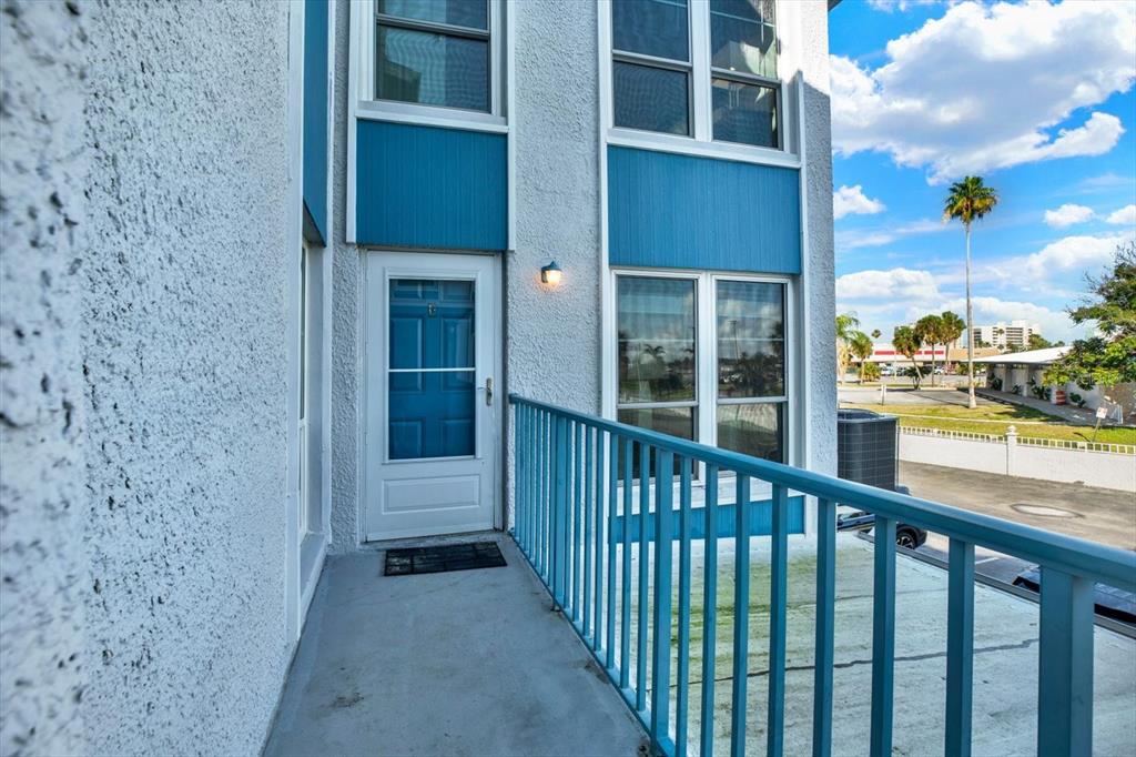 A blue-railed balcony leads to a white door on the exterior of a building — 169 MEDALLION BOULEVARD UNIT E, MADEIRA BEACH, FL