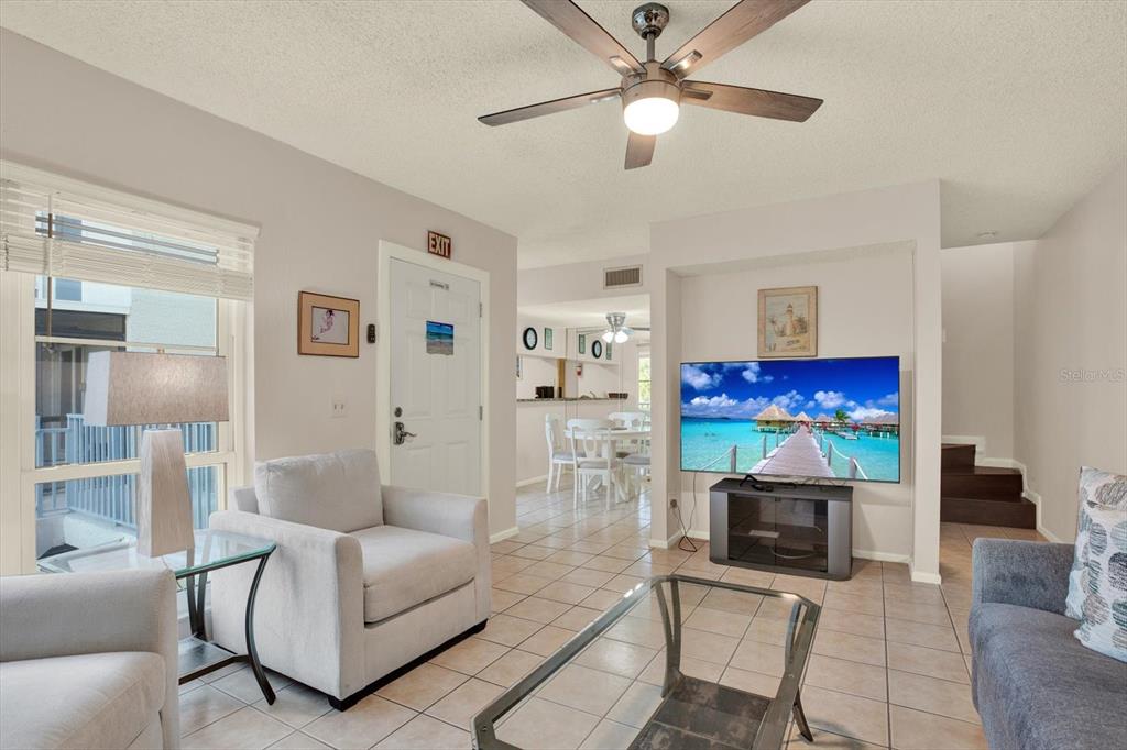 A living room with tile floors, a ceiling fan, and a television on a stand — 169 MEDALLION BOULEVARD UNIT E, MADEIRA BEACH, FL