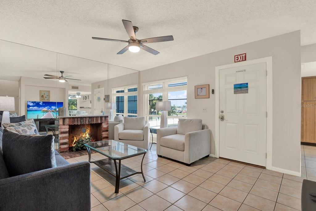 A living room features a brick fireplace, tiled floors, a ceiling fan, and mirrored walls — 169 MEDALLION BOULEVARD UNIT E, MADEIRA BEACH, FL