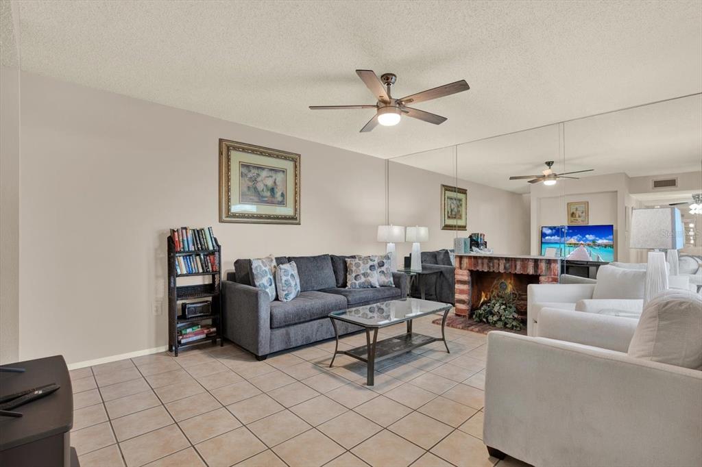 A living room features tile floors, a gray sofa, white armchairs, and a mirrored wall — 169 MEDALLION BOULEVARD UNIT E, MADEIRA BEACH, FL