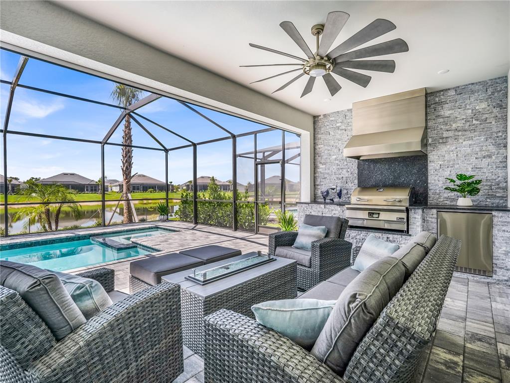 A covered outdoor patio features a stone grill station, wicker seating, and a screened pool — 44281 HENDERSON WAY, PUNTA GORDA, FL