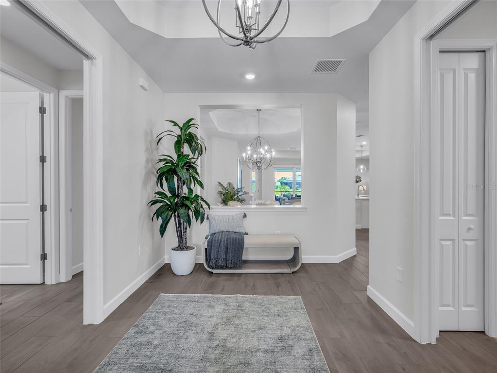 A bright foyer features gray wood-look flooring, a bench, a potted plant, and a chandelier — 44281 HENDERSON WAY, PUNTA GORDA, FL