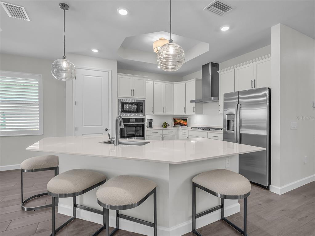 A modern kitchen features white cabinetry, stainless steel appliances, and a large quartz-topped island — 44281 HENDERSON WAY, PUNTA GORDA, FL