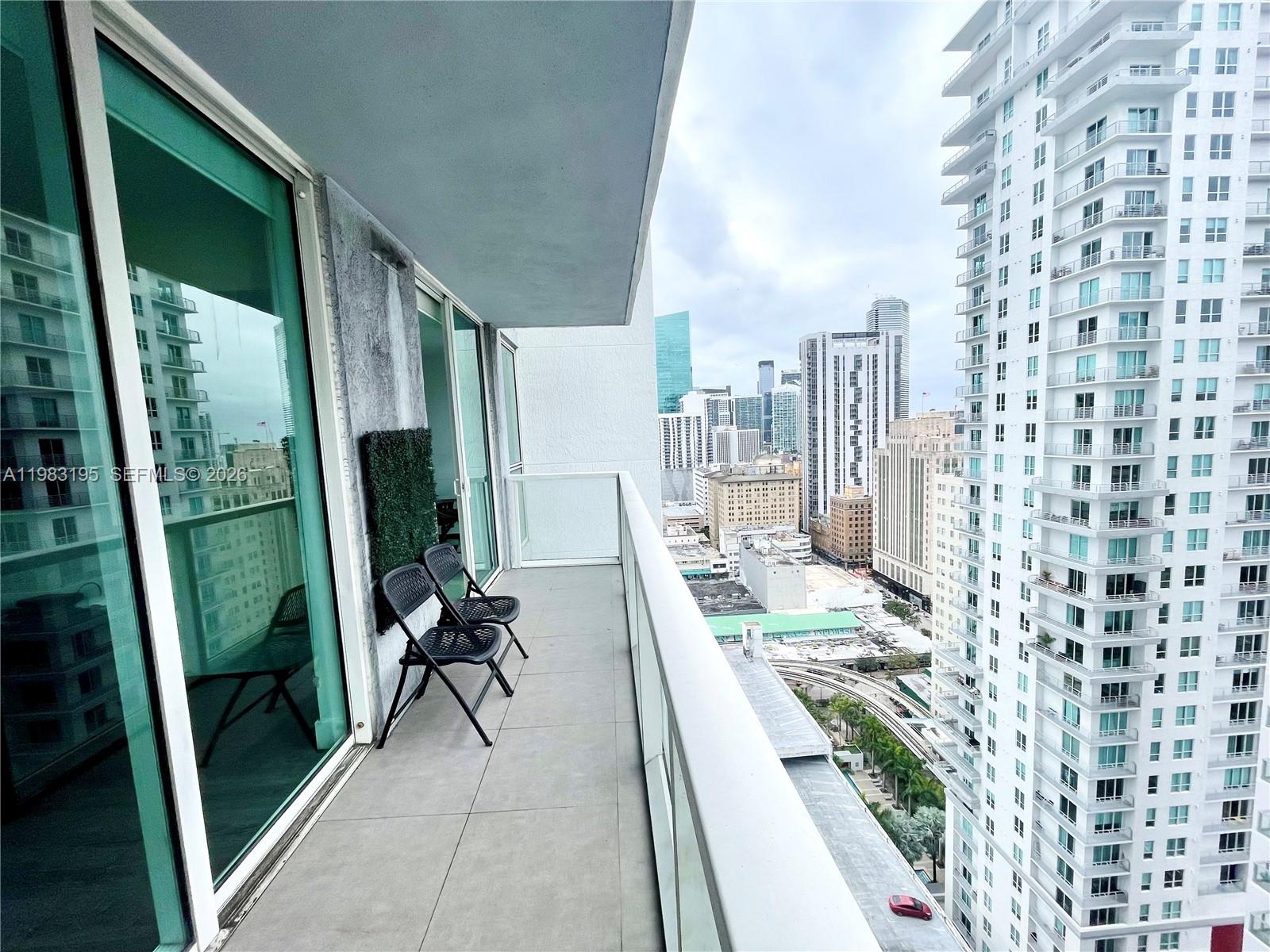 A balcony with two folding chairs overlooks a dense urban skyline of high-rise buildings — 253 NE 2nd St # 2506, Miami FL 33132, MIAMI, FL