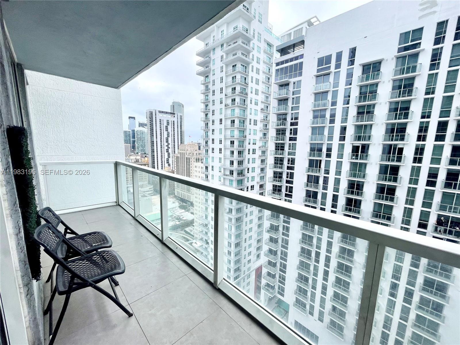 A balcony with two black chairs overlooks a dense urban skyline of high-rise buildings — 253 NE 2nd St # 2506, Miami FL 33132, MIAMI, FL