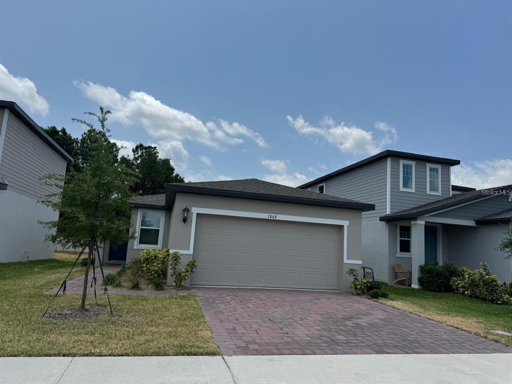 A single-story house with a beige stucco exterior, a two-car garage, and a paved driveway — 1868 CARNOSTIE ROAD, WINTER HAVEN, FL
