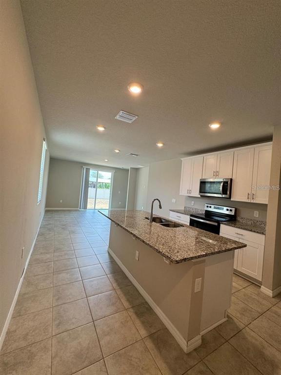 A kitchen with granite countertops and white cabinets overlooks an open-concept living area — 1868 CARNOSTIE ROAD, WINTER HAVEN, FL