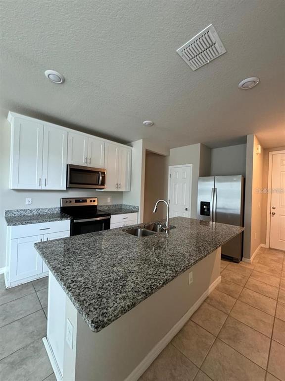 A kitchen features white cabinets, granite countertops, a center island with a sink, and appliances — 1868 CARNOSTIE ROAD, WINTER HAVEN, FL
