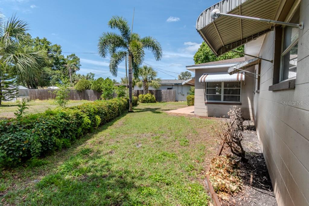 A grassy backyard features a hedge, palm trees, and the side of a house with awnings — 5800 21ST AVENUE S, GULFPORT, FL